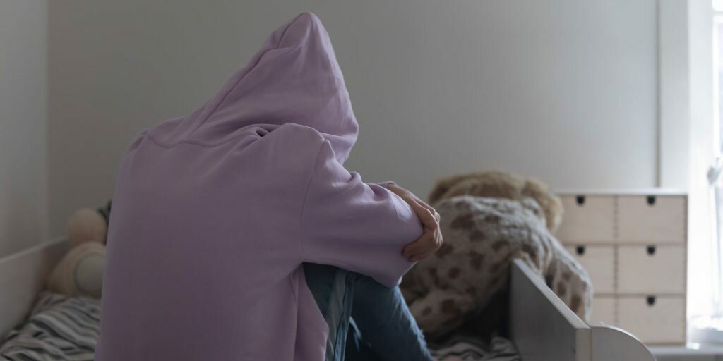 Young girl sitting on bed having suffered from trauma and at risk for addiction